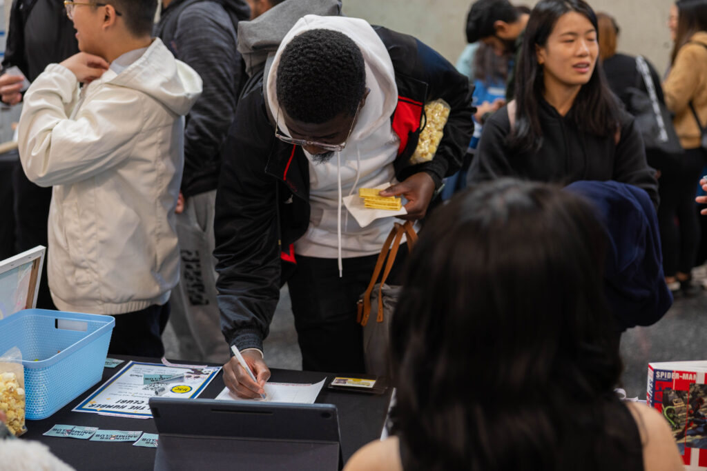 Student writing on a piece of paper on a table at the clubs fair. 