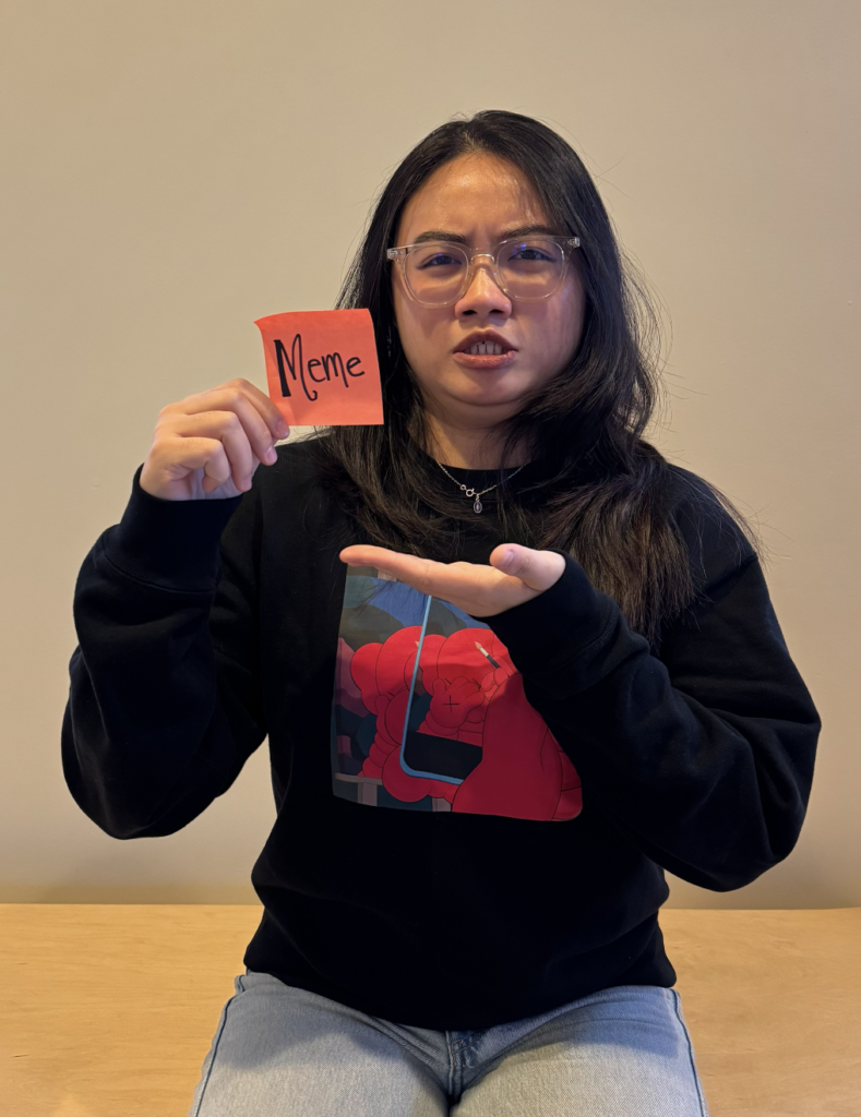 A girl holding a paper with a written word "Meme" that represents one of her talents.