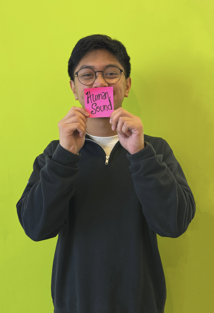 A boy holding a paper with a written word "Human Sound" that represents one of his talents.