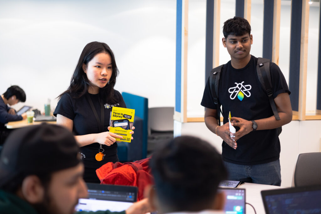 Two people are standing in a classroom, holding brochures. 