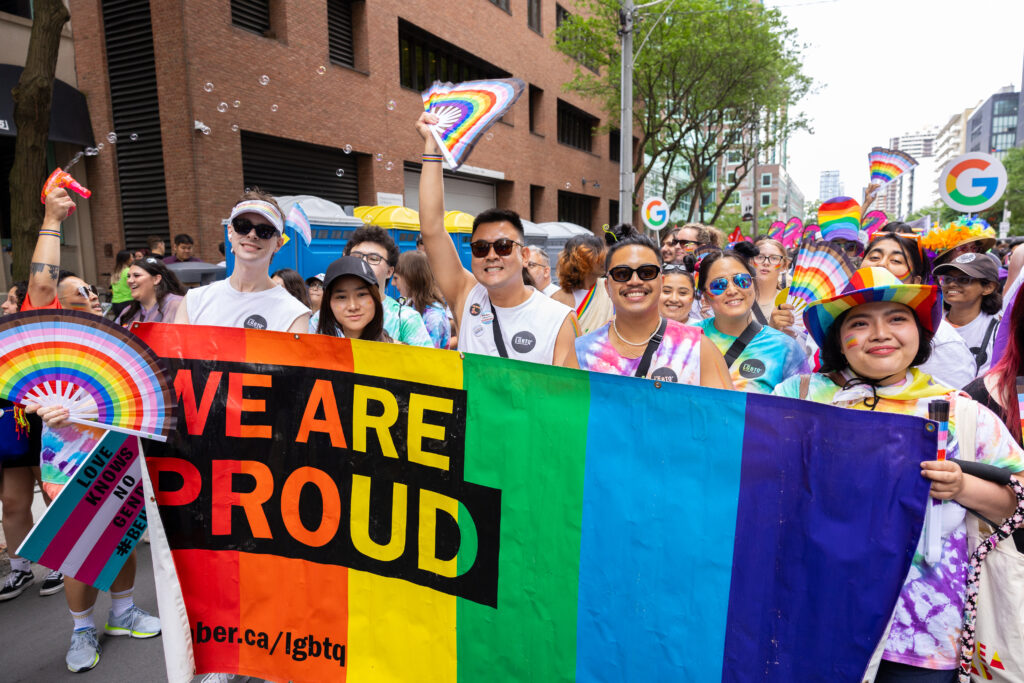 Image of people at the IGNITE Pride parade holding a Pride flag with text, "We are proud."