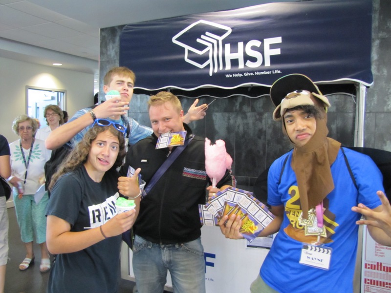A group of people is standing in front of the HSF stall, holding snacks and posing. 