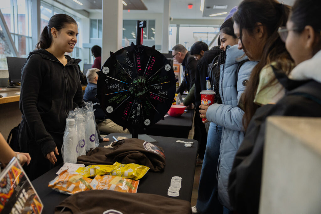 A woman is standing behind a counter, explaining a game to a group of students. 
