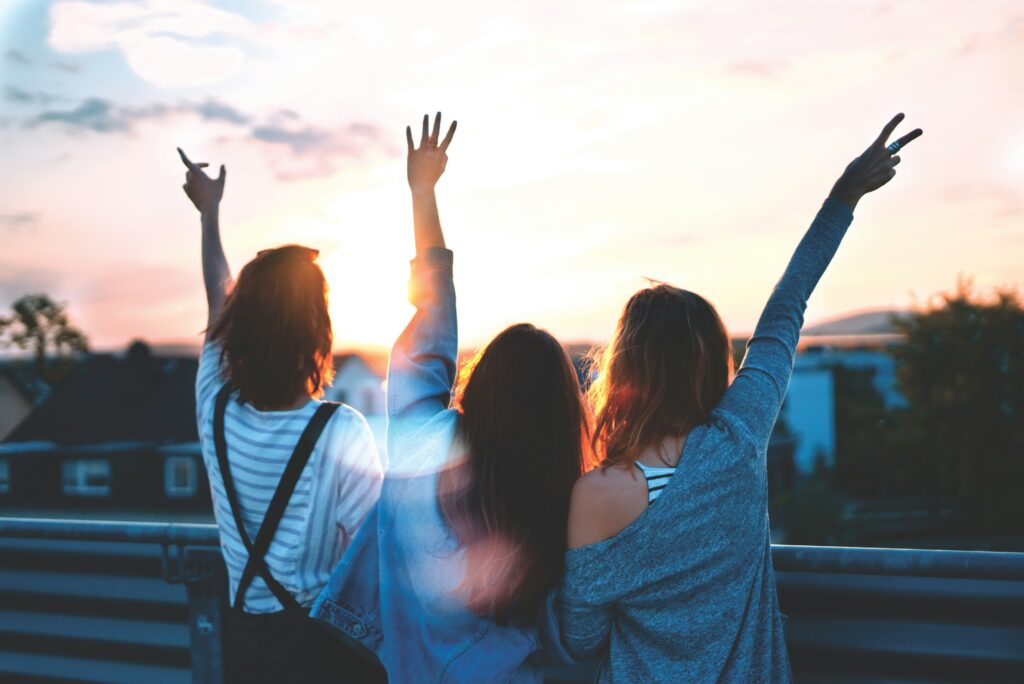 Three women with one arm up looking over a sunny city.