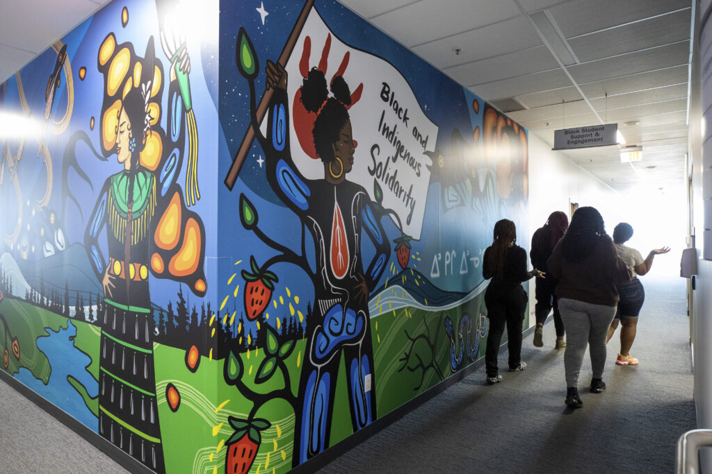A group of people walking beside a Black and Indigenous Solidarity mural at Humber.