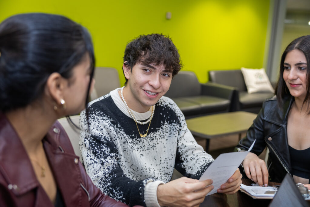 A man holding a piece of paper is looking at a woman with a smile on his face, while another woman is looking at him.