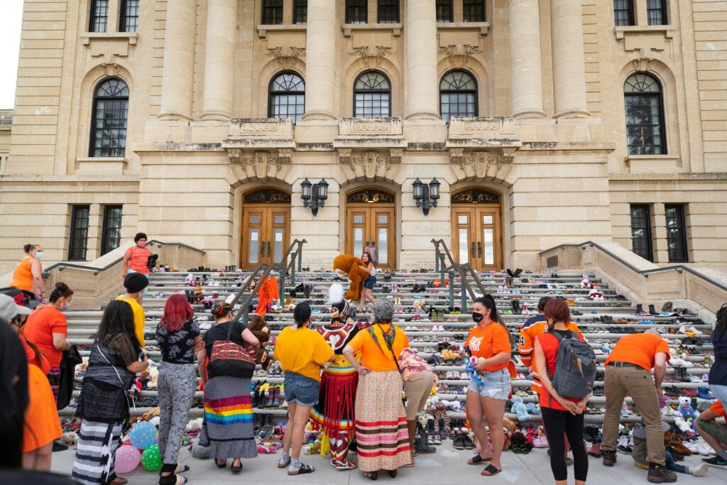 A group of people wearing orange in front of a building honouring the children who never returned home from the residential school system.