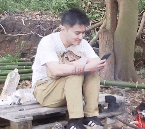 a man near a camp fire putting down his phone.