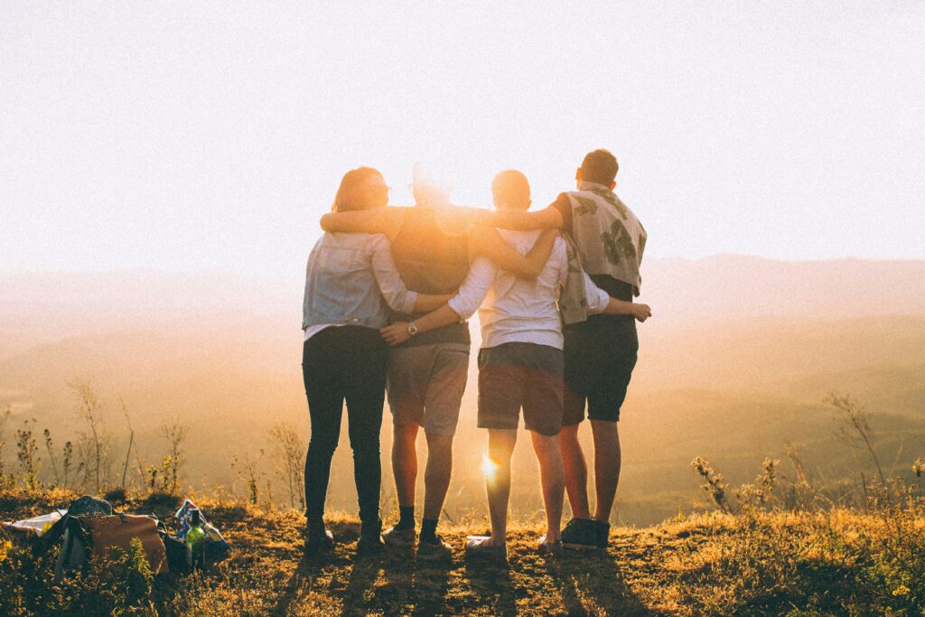 A group of friends hugging each other in the mountains as the sun sets.