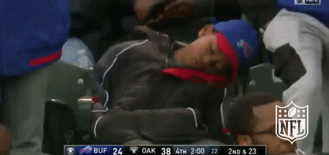 A kid sleeping at a stadium wearing a blue and red cap