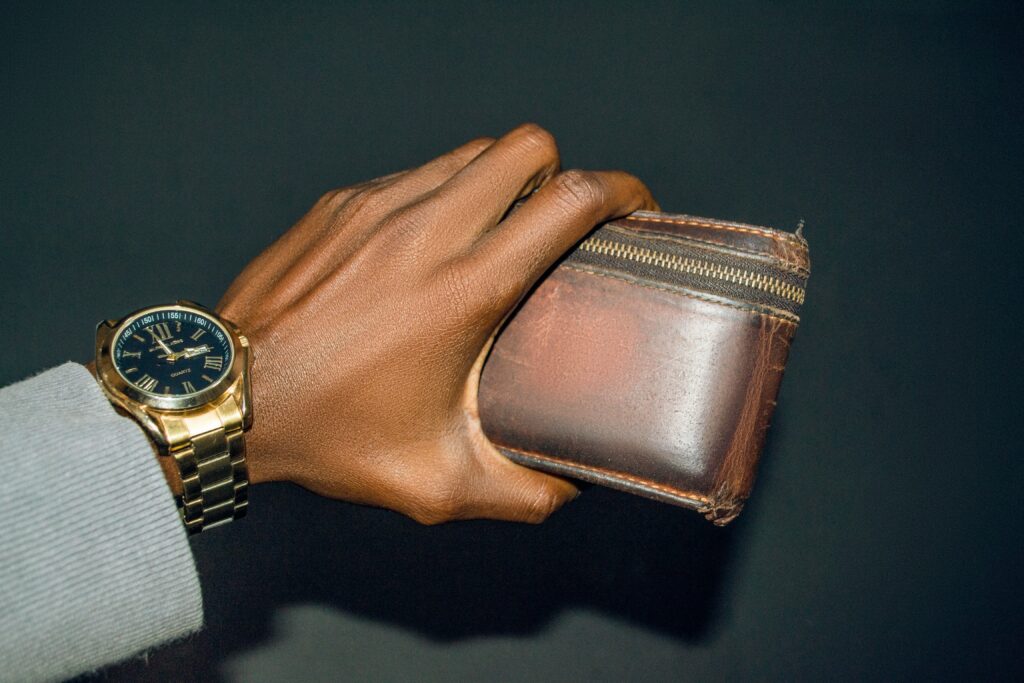 A hand with a gold watch and large brown wallet.
