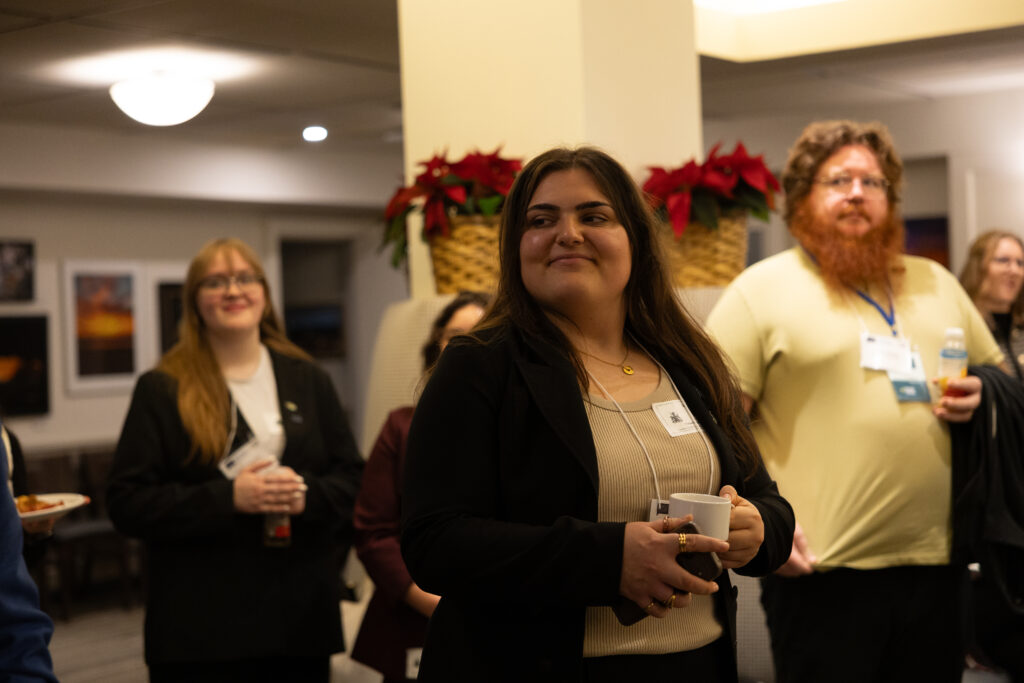 IGNITE Student Advocate Selena Ferreira is holding a mug and smiling, with Emily Edwards in the background.