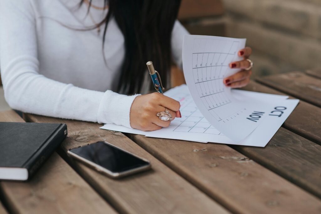 A person organizing in their physical calendar on a wooden park desk. 