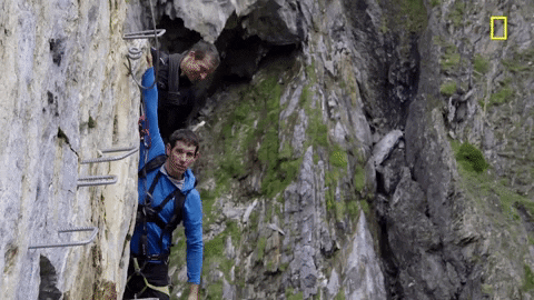 A man flexing while on a mountain rock climbing