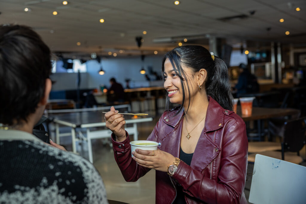 A girl wearing a red leather jacket is enjoying soup from the IGNITE  Soupbar.