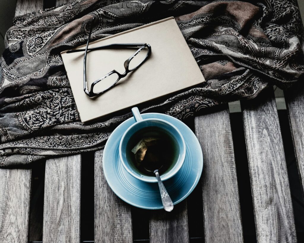 A cup of tea in front of a notebook with glasses on top of it.