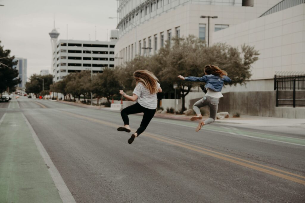 Two people jumping in the air and clapping their heels together in the middle of the street.