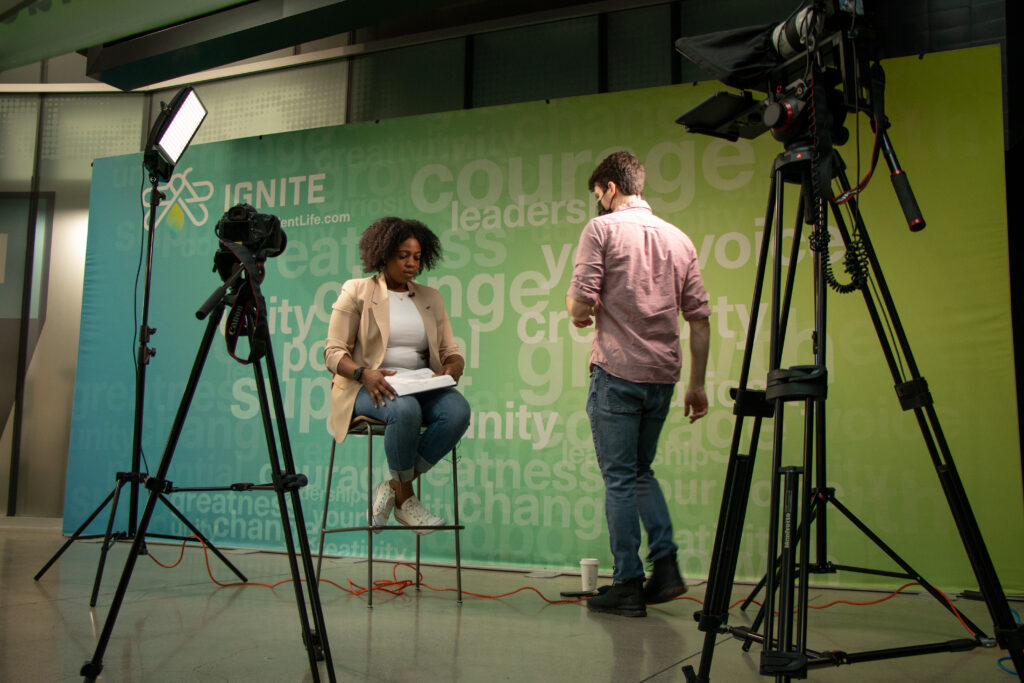 A videographer preparing for a shoot with two cameras and a large light in the student centre at the North campus.