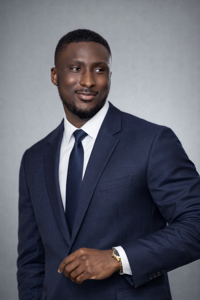 A headshot of Akwasi Boateng with an all blue suit, white dress shirt and gold watch. 