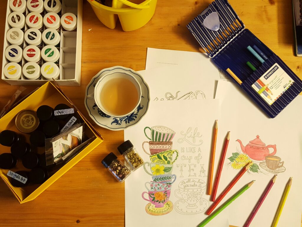 A top shot image of colour pencils, paints and a tea
