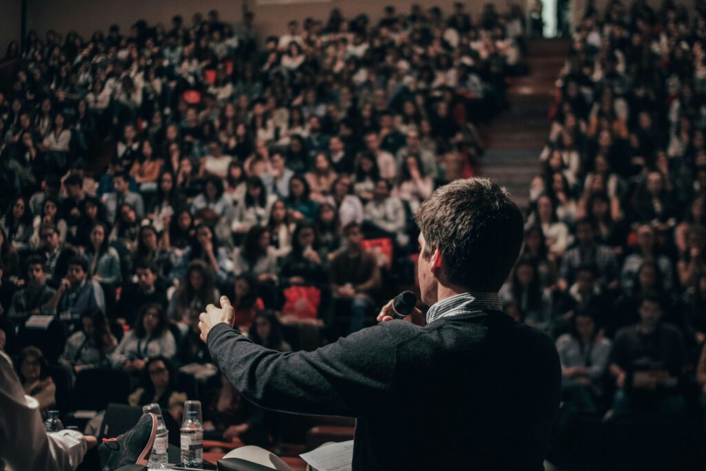 A man's back facing a large crowd as he talks into a mic